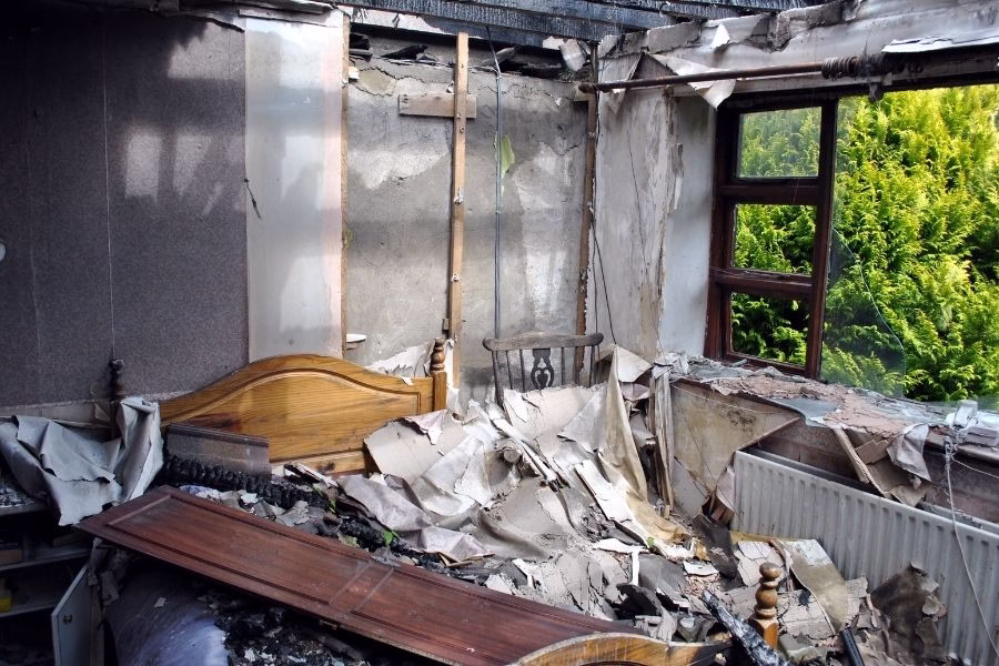 Bedroom interior with severe fire and smoke damage showing charred walls and destroyed furniture