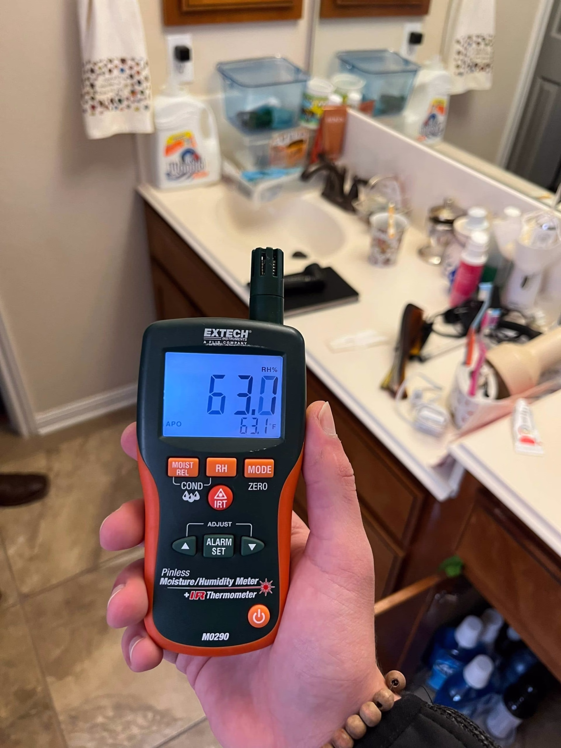 Moisture meter being used to measure moisture levels in bathroom wall during mold assessment