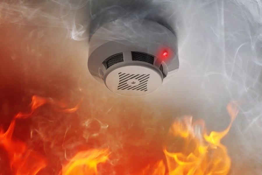 Smoke detector with alarm light surrounded by flames and thick smoke in a home in Austin TX