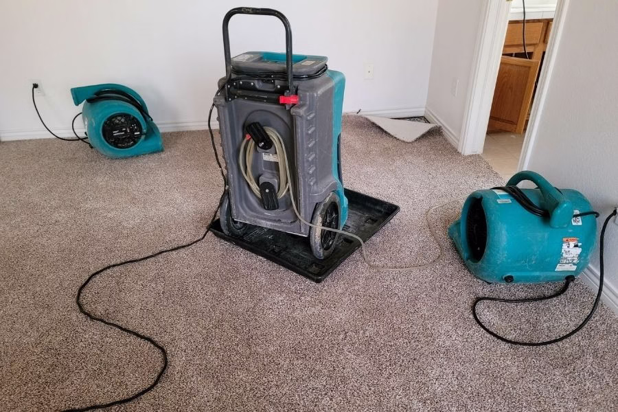 Air movers and dehumidifiers staged in a residential kitchen after water heater burst, cabinet doors removed to allow airflow behind units