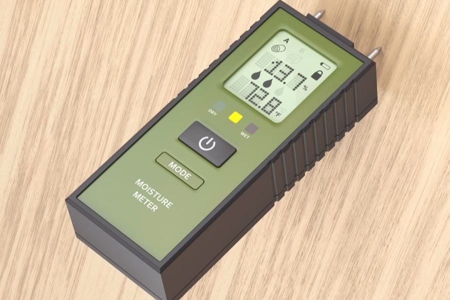 Technician taking a moisture reading on exposed plywood subfloor with hardwood flooring removed, commercial drying equipment running in the background