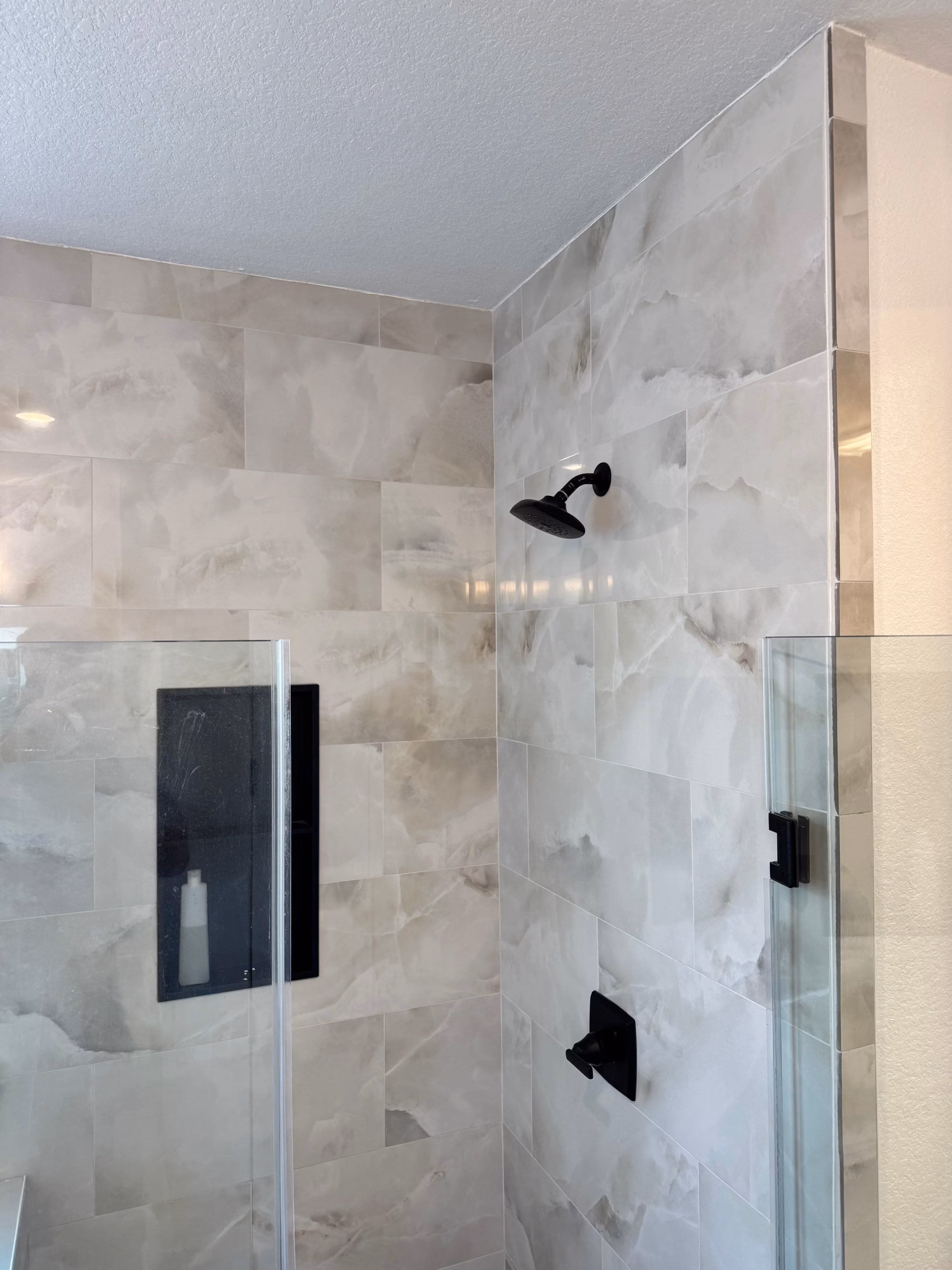Restored walk-in shower with marble-look tile after water damage rebuild