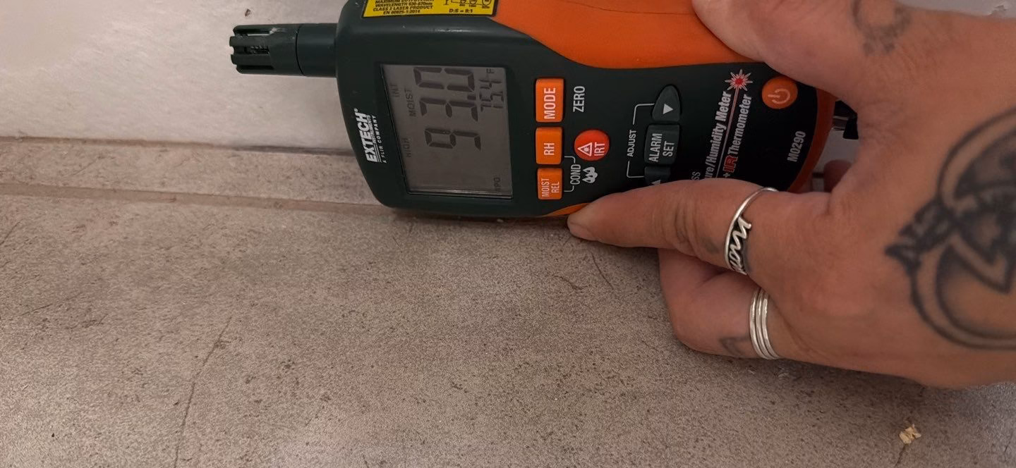 Moisture meter reading on damp hallway carpet and baseboard during a Leander water damage inspection