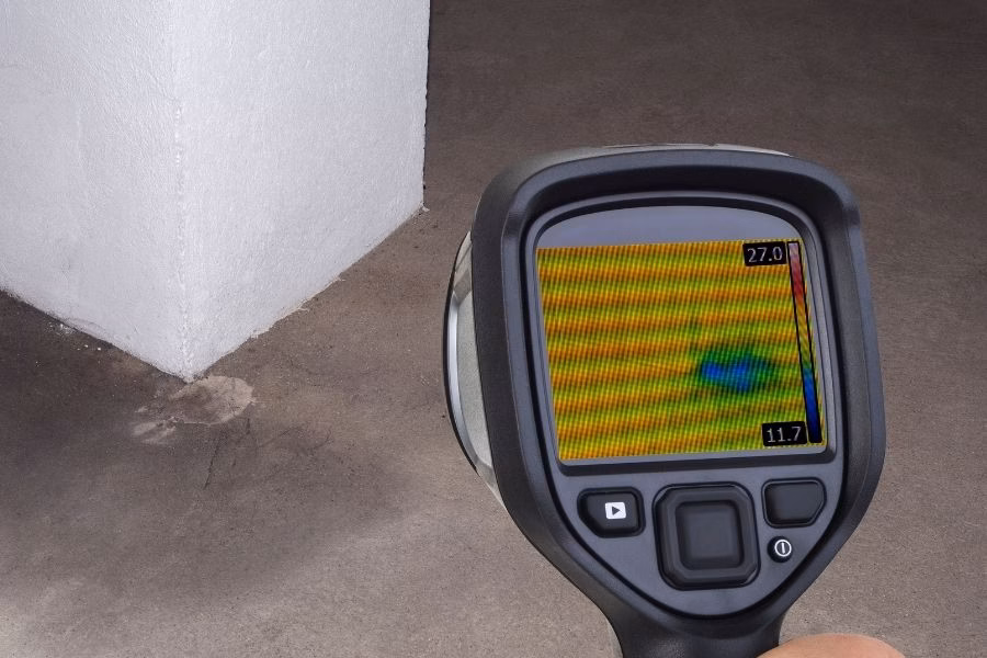 Thermal imaging camera scanning a wall corner and detecting a cool spot that points to hidden moisture