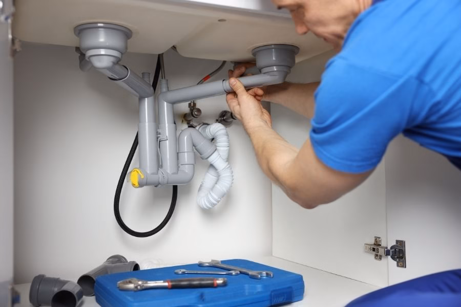 Worker checking the drain pipes and P trap under a kitchen sink for leaks with tools laid out nearby