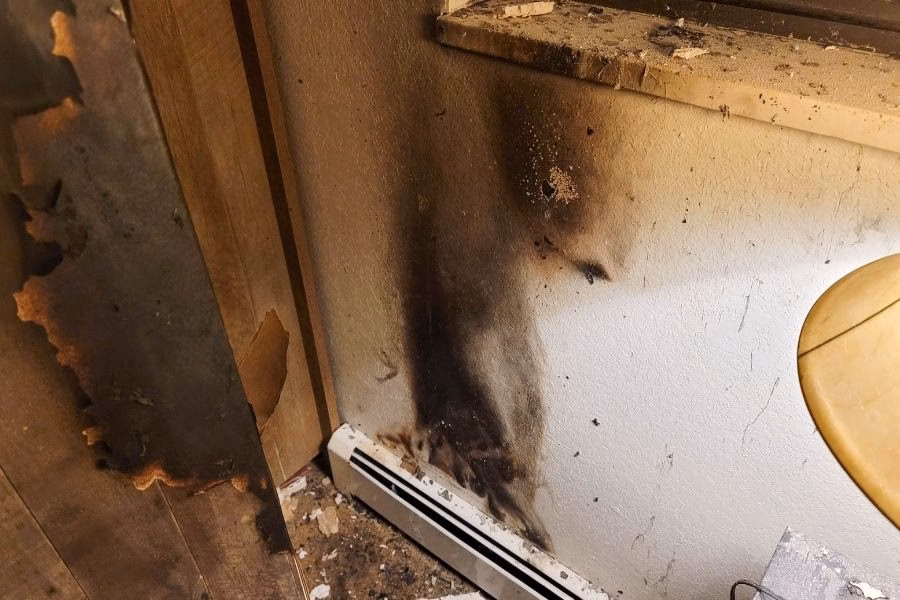 Black soot staining climbing a wall and door frame above a baseboard heater after a house fire